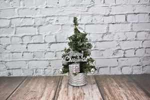 Close-up of mini Christmas tree with silver ornaments and Merry Christmas sign in a silver basket