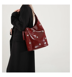 Detail of burgundy patent leather hobo bag with silver studs on a black blazer