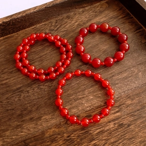 Close-up of red agate beaded bracelets in three sizes on a rustic wooden tray
