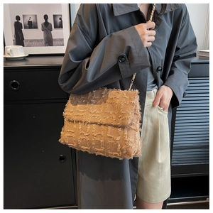 Close-up of beige woven shoulder bag with fringe texture and elegant metal chain strap