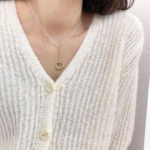 Detail of a mixed-tone heart pendant necklace worn on a cream-colored knit cardigan