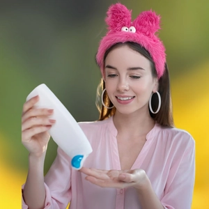 White skincare bottle with blue cap held by model on yellow and green background