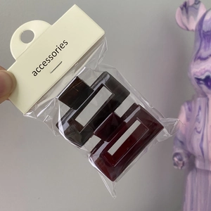 Deep red brown geometric hair clips in card packaging held against a neutral wall