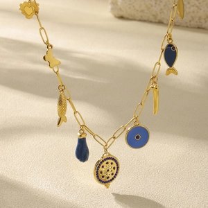 Collier chaîne dorée avec breloques cœur, papillon, poisson et œil bleu sur fond beige doux