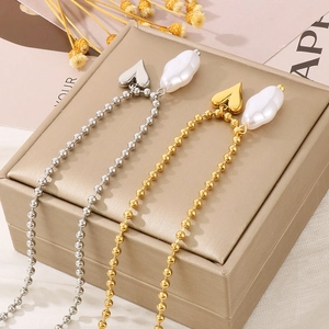 Detailed view of gold and silver ball chains with heart pendants and baroque pearls