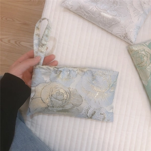 Detail of light blue rose jacquard canvas mini wristlet bag with gold floral patterns