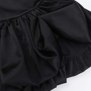 Close-up of the black satin fabric texture with ruffled edge and pleated dress details