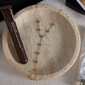 Detailaufnahme einer goldfarbenen Türkis-Bodychain auf einem beigen Steintablett