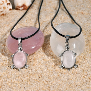 Détail de deux pendentifs tortue avec pierres naturelles sur un fond de plage de sable