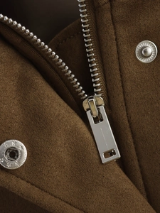 Détail de la fermeture éclair argentée et du bouton-pression sur veste marron