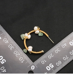 Detail view of handmade C-shape hoop earrings with white pearls and green stones on a scale