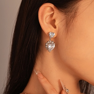Close-up of a silver heart drop earring with sparkling zircon stones on a model's ear