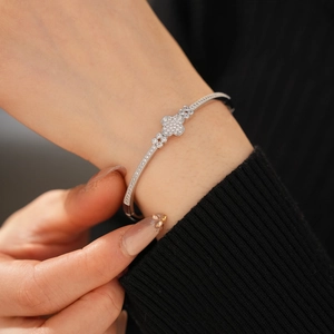 Close-up of sparkling zircon-encrusted clover bangle on a model's wrist with black sweater