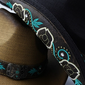 Detailed macro view of western straw hat with ethnic blue embroidery and metal buckle