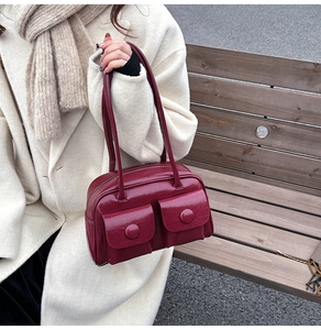 Close-up of a vintage burgundy shoulder bag with dual front pockets on a model