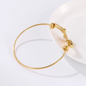 Golden stainless steel coin and heart charm bracelet displayed on a white ceramic plate