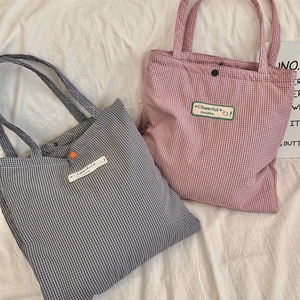 Detail view of plaid canvas tote bags with metal snap button and embroidered logo label