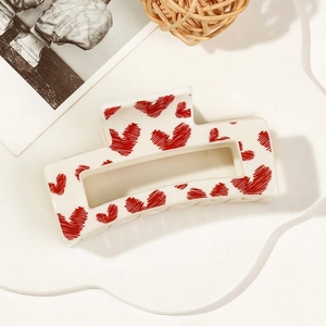 Detail of cream rectangular hair claw clip with red heart patterns and hollow center design