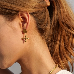 Close-up of vintage gold cross earrings with textured metal and natural stone inlay
