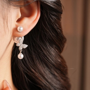Macro shot of silver butterfly earrings with zircons and pearls worn by a model