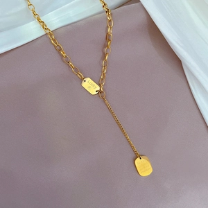 Detail of gold titanium Y-necklace with Lucky brand rectangular pendants on fabric