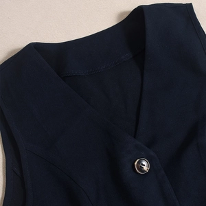 Dettaglio cuciture scollo a V e bottoni ambrati sul set gilet tessuto blu scuro