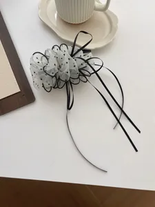 Detail of white mesh hair clip with black polka dots and flowing satin ribbons on a desk