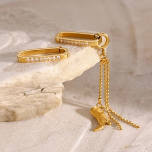 Detail of gold U-shaped earrings with zircon accents and a tiny boot charm on stone