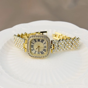 Close-up of luxury gold square watch with shimmering crystals on a white ceramic plate