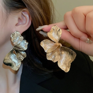 Detailed close-up of large golden floral stud earring with brushed metal texture