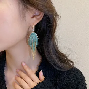 Elegant U-shaped tassel earrings with turquoise rhinestones and gold chains on model