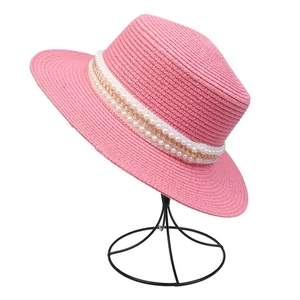 Close-up of pink straw hat with elegant pearls and golden chain on a display stand