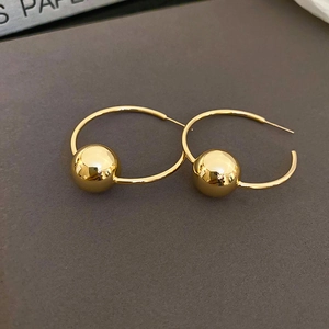 Dettaglio di orecchini a cerchio in oro lucido con pendente a sfera su sfondo grigio