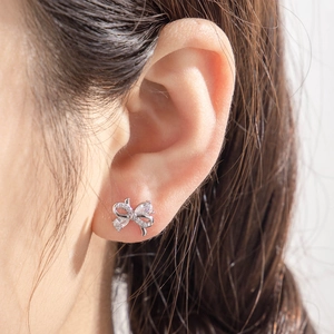 Elegant silver bow stud earrings with sparkling crystals shown on a model's ear