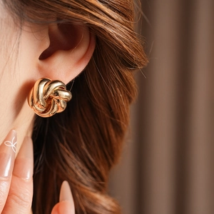 Close-up of elegant gold twisted swirl flower stud earrings worn by a model