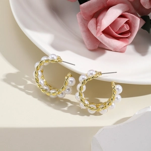 Detailed view of elegant gold twisted hoop earrings with white pearls on a white plate