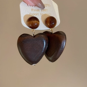 Détail des boucles d'oreilles en bois en forme de cœur avec perle œil de tigre et cuivre