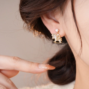 Detail of elegant gold horse stud earring with white enamel and pearl on female ear