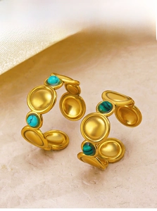 Detail of gold plated ring with inlaid turquoise and malachite on a beige surface