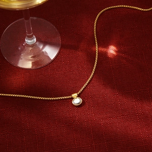 Dettaglio collana in oro con pendente in zircone tondo su lussuoso tessuto rosso