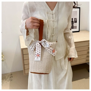 Détail du sac seau en paille beige avec poignée en cuir marron et foulard en soie décoratif