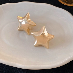 Close-up of high-polish golden star stud earrings on a decorative white porcelain tray