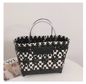 Detail of woven straw tote bag featuring black and white geometric pattern and round handles