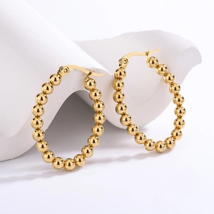 Detail of gold beaded oval hoop earrings featuring a high-polish spherical texture design
