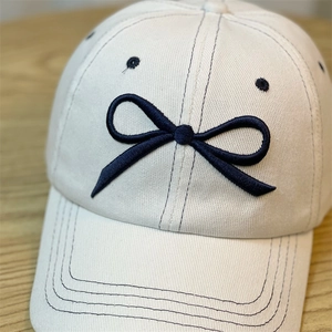 Close-up of cream baseball cap with navy blue bow embroidery on twill fabric