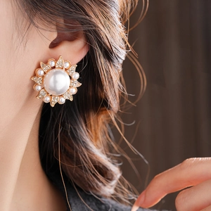 Close-up of pearl flower stud earrings with crystals worn by a model in soft light