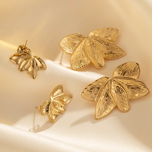 Detail of gold leaf earrings with realistic vein texture on beige satin background