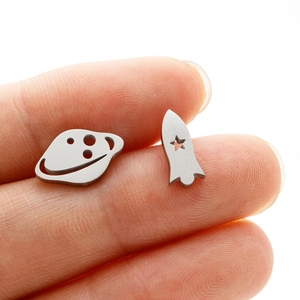Close-up of asymmetrical silver rocket and planet stud earrings on a fingertip