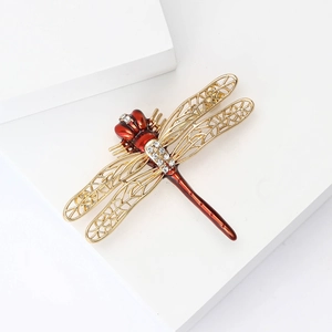 Elegant gold dragonfly brooch with red enamel and crystals on white geometric stands
