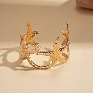 Detailed close-up of a gold starfish open bangle with authentic shell texture on sand